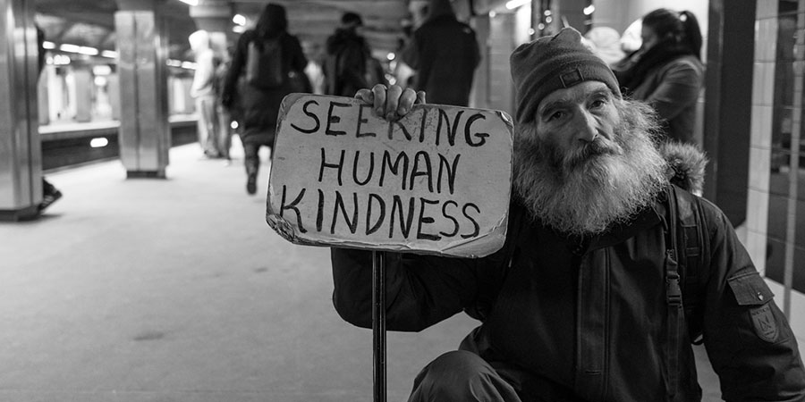 man with white beard holding a cardboard with the words "seeking human kindness"